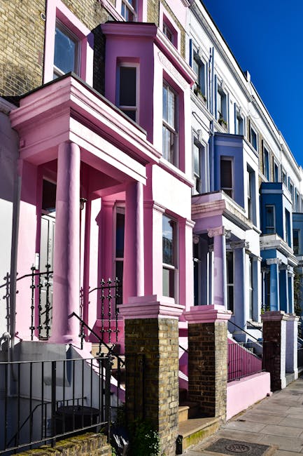 Exterior view of a row of colorful residential buildings in Notting Hill, featuring pastel facades in shades of pink, yellow, blue, and white. The buildings have multiple large sash windows with white